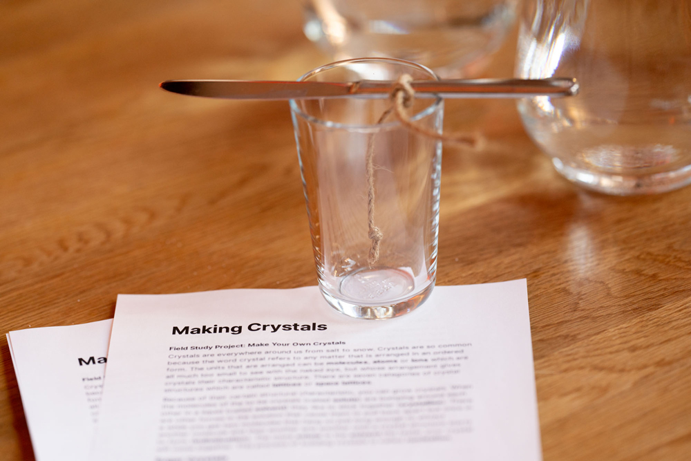 A glass with a string suspended from a knife, over the Making Crystals guide